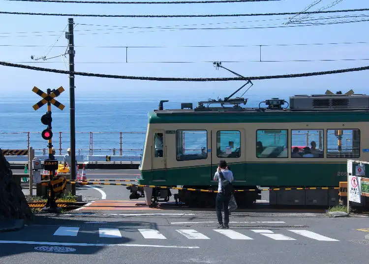 鎌倉高校前駅の踏切で江ノ電が通過する様子。スラムダンクの聖地として有名な湘南海岸のアニメ巡礼スポット。