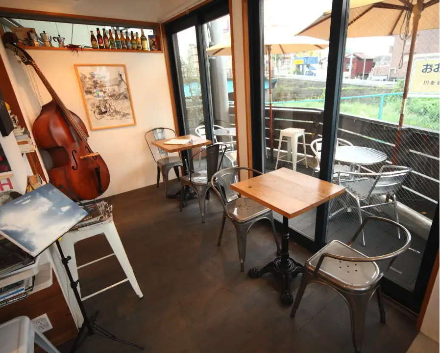 Cafe de Fleurus 27の店内。ウッドベースが置かれた音楽好きにぴったりの空間と、川沿いのテラス席が見えるガラス窓。